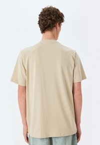Kortærmet t-shirt med rund hals i lys beige, lavet af blødt bomuld. Har en glat tekstur og en lige kant, uden udsmykninger.