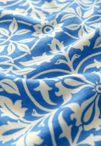 Blåt stof med hvid blomsterpatter, der har blade og blomster, glat tekstur med let drapering.