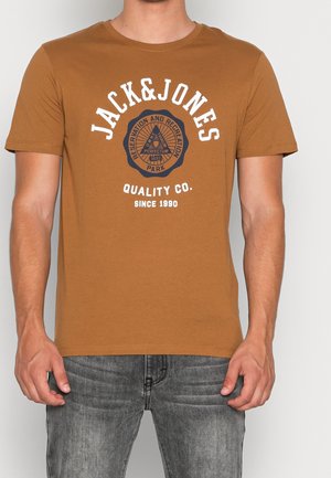 T-shirt en coton brun avec un col rond. Le devant présente un logo graphique bleu avec un texte blanc indiquant "JACK & JONES" et "QUALITY CO."