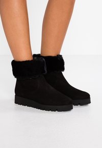 Botas de tobillo de ante negro con un puño de pelo sintético, con puntera redondeada y suela de goma texturizada para mayor tracción.