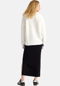 Vit oversized tröja med långa ärmar, i kombination med en svart maxiklänning med sprund på sidan, och svarta sneakers med vita ränder.