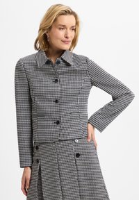 Houndstooth-patterned jacket featuring a collar, black buttons, and two front pockets. Textured fabric with a fitted silhouette.