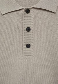 Beige knit polo with a ribbed texture, featuring a classic collar and three black buttons down the front.
