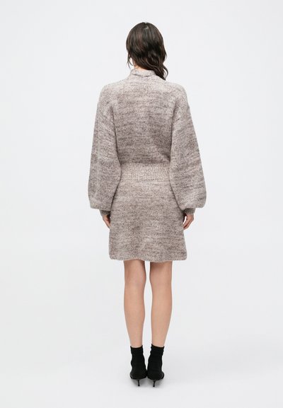 Pletené šaty v svetlo hnedej a krémovej farbe s dlhými balónovými rukávmi, priliehavým pásom a voľnou sukňou, doplnené čiernymi členkovými ponožkami a lodičkami.