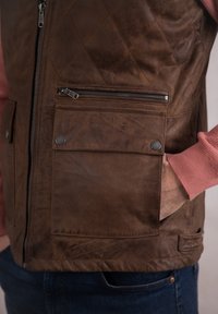 Brown leather vest with diamond quilted pattern, featuring a zippered pocket and a buttoned flap pocket. Pink sweater visible underneath.