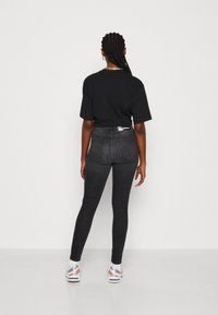 Camiseta negra de corte suelto; jeans negros ajustados de cintura alta con bolsillos traseros; color sólido con una textura suave; combinados con zapatillas deportivas.