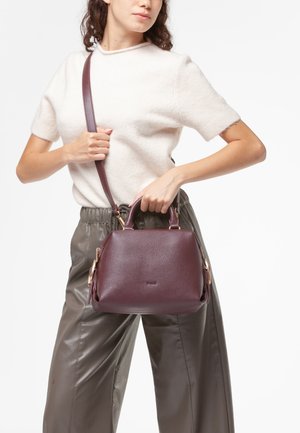 Borsa a mano in pelle color bordeaux con forma arrotondata, doppi manici e tracolla. Presenta finiture in metallo dorato e una superficie texturizzata.