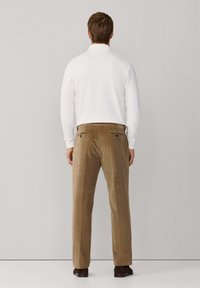 Witte, lange mouwen polo met bruine corduroy broek met verticale strepen, twee achterzakken en donkerbruine schoenen.