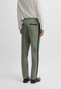 Green plaid trousers with black side stripes, featuring a tailored fit, back pockets, and a flat waistband. Worn with a white dress shirt.