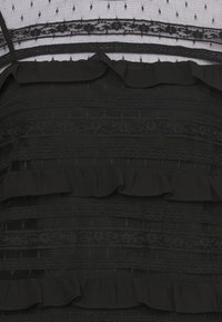 Tessuto nero a strati con righe orizzontali di pizzo e volant; la rete trasparente con un motivo a pois arricchisce la texture e il design.