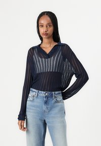 Blusa de rayas marinas de manga larga con cuello y detalle de botones, combinada con jeans de tiro alto en azul claro. Textura transparente.