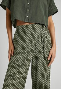 Olijfgroen cropped blouse met knopen, gecombineerd met geweven broek met een geometrisch patroon in lichter groen.