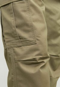 Khaki cargobroek van een gestructureerde stof, met zijzakken en zichtbare stiksels. Duidelijke plooien en vouwen zichtbaar.