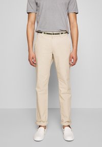 Beige cotton chinos with a straight cut, featuring front pockets and rolled cuffs, paired with a gray t-shirt and white slip-on shoes.