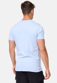 T-shirt in cotone azzurro chiaro con maniche corte e colletto a girocollo. Presenta una texture liscia e cuciture laterali visibili. Pantaloni cargo neri indossati.