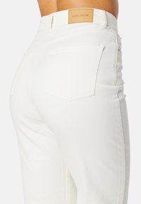 Witte denim jeans met een aansluitend ontwerp, voorzien van twee achterzakken, een leren label met "BUBBLEROOM" en gestikte naden langs de zijkanten.