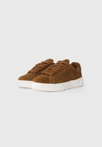 Brown suede sneakers with a low-profile design, featuring a white rubber sole, round laces, and a small logo in gold on the side.