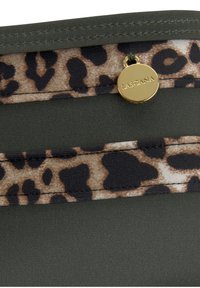 Zaļš auduma maisiņš ar leoparda rakstu, ar zelta detaļu, kurā ir uzraksts "LASCANA." Gluda tekstūra ar redzamām šuvju detaļām.
