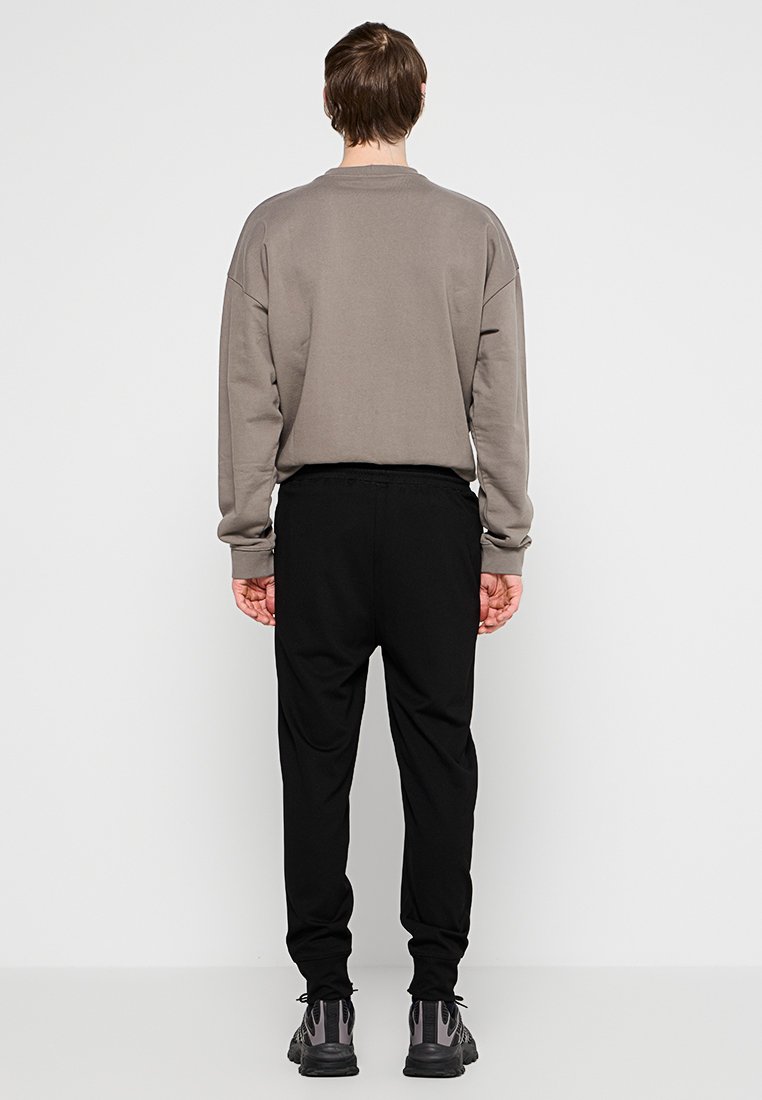 Grå sweatshirt med sänkt axel, ihopparad med svarta tapered byxor. Texturerad tyg och elastiskt midjeband; bärs med mörka sneakers.