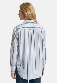 Light blue striped shirt featuring vertical black and thin cyan lines, long sleeves, back pleat, and curved hem. Buttoned cuffs.