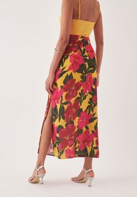 Geel bloemenmaxi rok met grote roze bloemen en groene bladeren, met een zijsplit. Gecombineerd met zilveren hoge hak sandalen.