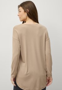 Beige langærmet top med en afslappet pasform, glat tekstur, rund sømkant og subtile sømdetaljer ved skuldrene og manchetterne.