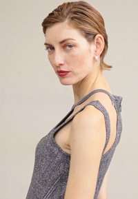 Szürke, ujjatlan ruha fénylő textúrával és aszimmetrikus vállpántokkal. Hátul nyitható zipzárral és testhezálló sziluettel rendelkezik.