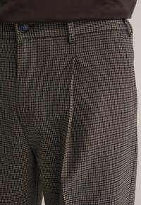 Brązowe spodnie w kratę o teksturowanym wykończeniu, z zapięciem na guzik, przednimi kieszeniami oraz zwężanym krojem.
