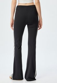 Leggings évasés noirs en tissu extensible avec des rayures latérales blanches. Présente une taille lisse et un design élégant et ajusté.