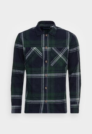 Chemise à manches longues avec boutons, à grand motif à carreaux vert, marine et blanc, avec deux poches sur la poitrine.
