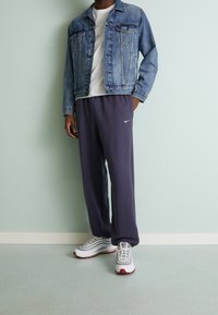 Sininen farkkutakki etutaskuilla, valkoinen t-paita, harmaat collegehousut, joissa on Nike-logoa, ja valkoiset/punaiset urheilukengät.