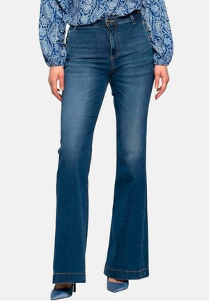 Jeans in denim scuro a gamba svasata con vita alta, caratterizzati da una superficie liscia e dettagli di cucitura sottili, abbinati a una maglietta blu stampata.