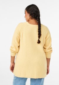 Maglione giallo chiaro lavorato a maglia con vestibilità ampia, maniche a raglan e trama a coste. Presenta un orlo posteriore basso e maniche con polsini arrotolati.