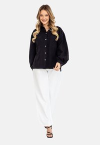 Czarna koszula na guziki z dwoma kieszeniami na piersi, z balonowymi rękawami i luźnym fasonem, w połączeniu z białymi spodniami o szerokich nogawkach i czarnymi sandałami na obcasie.