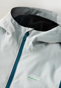 Hellgraue Jacke mit einem fleecegefütterten Kapuzen, ausgestattet mit einem blauen Reißverschluss und Logodetail. Glattes, strukturiertes Gewebe mit präziser Nahtführung.