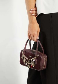 Burgundy leather handbag with a structured shape, dual handles, gold chain accents, and decorative charms attached to the front zipper.