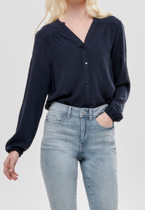 Blouse marine en tissu lisse, avec un col en V, une fermeture à boutons et des manches longues. Associée à un jean taille haute bleu clair.