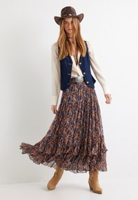 Falda larga con estampado y volantes en azul, naranja y crema. Combinada con un chaleco de mezclilla y un sombrero de cowboy marrón, acentuada con una hebilla de cinturón plateada.