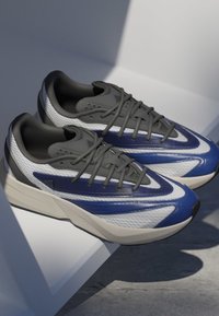 Multi-colored athletic sneakers featuring a white mesh upper with blue and grey accents, grey laces, and a textured sole for grip.