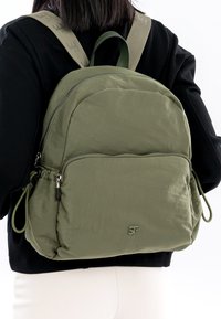 Olijfgroene rugzak met een zachte, gekreukte textuur, voorzien van ritsvakken, verstelbare bandjes en subtiele logodetails.