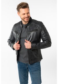 Schwarze Lederjacke mit tailliertem Design, ausgestattet mit gesteppten Schulterakzenten und zwei Reißverschlusstaschen auf der Brust. Glatte Textur.