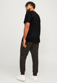 Schwarzes T-Shirt mit kurzen Ärmeln, kombiniert mit schwarzen schmalen Jogginghosen und weißen Sneakers. Der Stoff wirkt glatt und lässig.