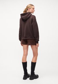 Hanorac maro supradimensionat cu glugă, asortat cu pantaloni scurți maro. Botine negre până la genunchi completează ținuta. Material neted și croială lejeră.
