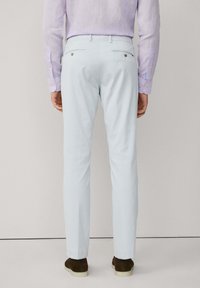Hellblaue Hose mit glatter Textur, schlankem Schnitt und zwei Gesäßtaschen. Kombiniert mit einem lila Langarmhemd und braunen Schuhen.