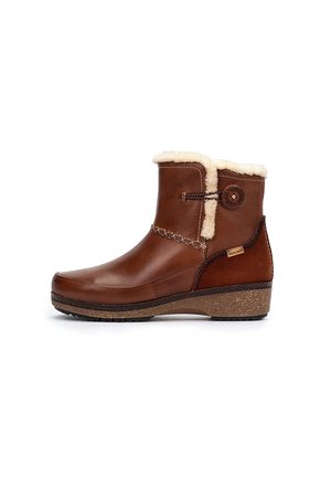 Botas de cuero marrón hasta el tobillo con un cuello de pelo sintético, costuras decorativas y una suela de corcho texturizada. Acento del logo metálico en el costado.