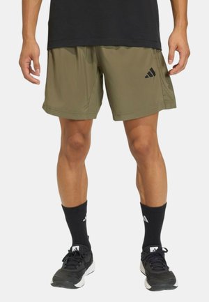 Uomo che indossa pantaloncini sportivi verde oliva con logo nero, calzini sportivi neri e scarpe da corsa nere, in piedi su sfondo bianco.