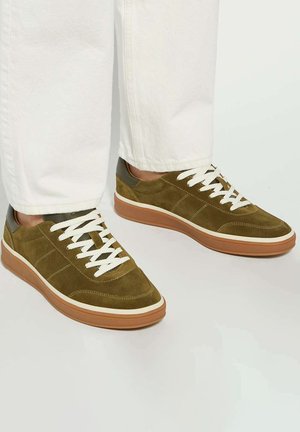 Olive green suede sneakers with white laces, light brown rubber sole, and contrasting dark accents on heel. Flat, rounded toe design.