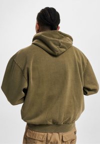 Hoodie en coton vert olive avec une grande capuche, des poignets côtelés et une coupe décontractée. Tissu texturé au design simple.