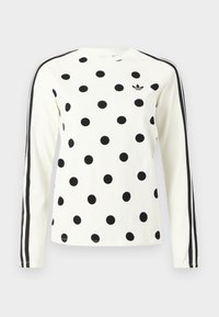 Valge pikamaa särk mustade täppidega, must Adidas logo rinnal ja kaks musta triipu kummalgi varrukal.