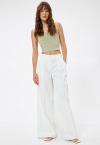 Top corto ajustado de color verde claro y pantalones de pierna ancha blancos con pliegues frontales. La modelo está de pie frente a un fondo sencillo, mostrando la simplicidad del atuendo.